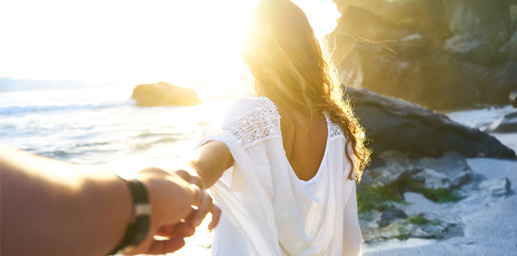 person holding woman's hand beside sea while facing sunlight