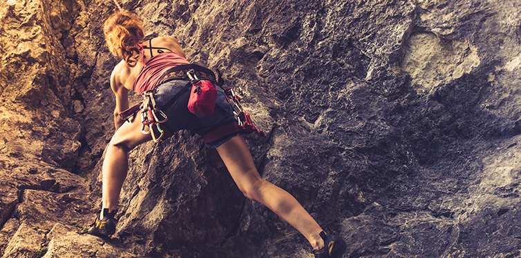 аthletic woman rock climbing at sunset in climbing apparel