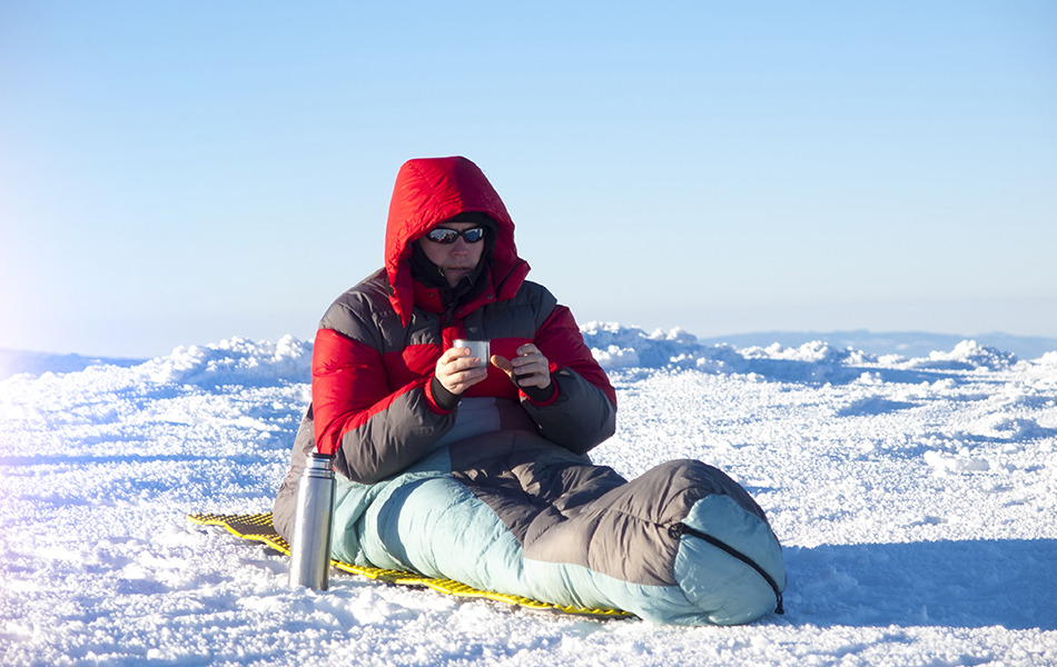 a man sits in a sleeping bag and drinking tea