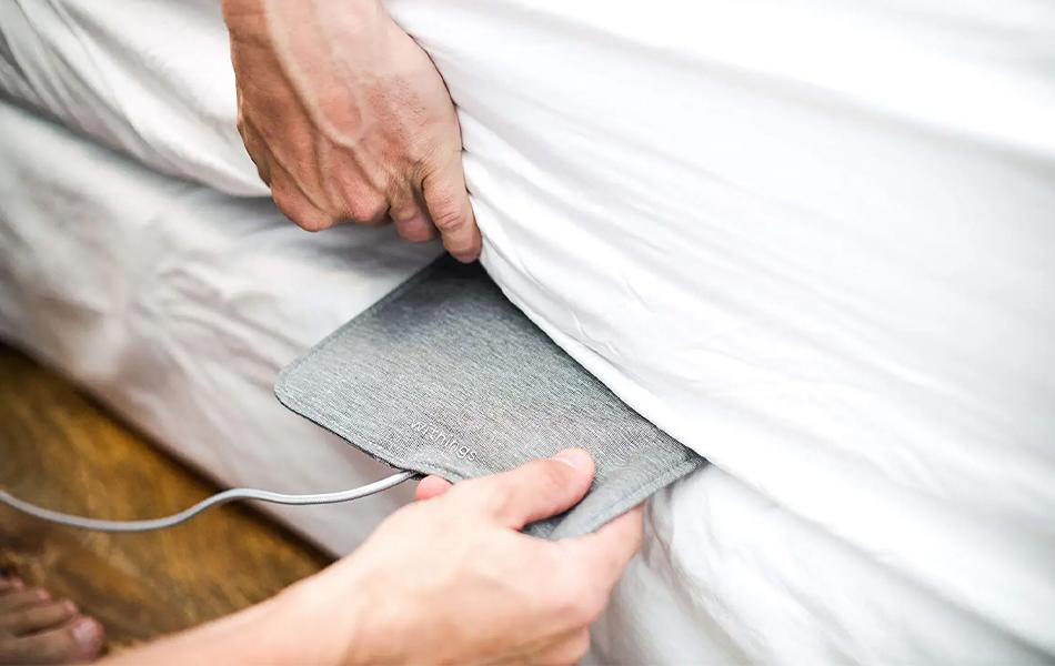 man placing sleep tracking pad under the mattress