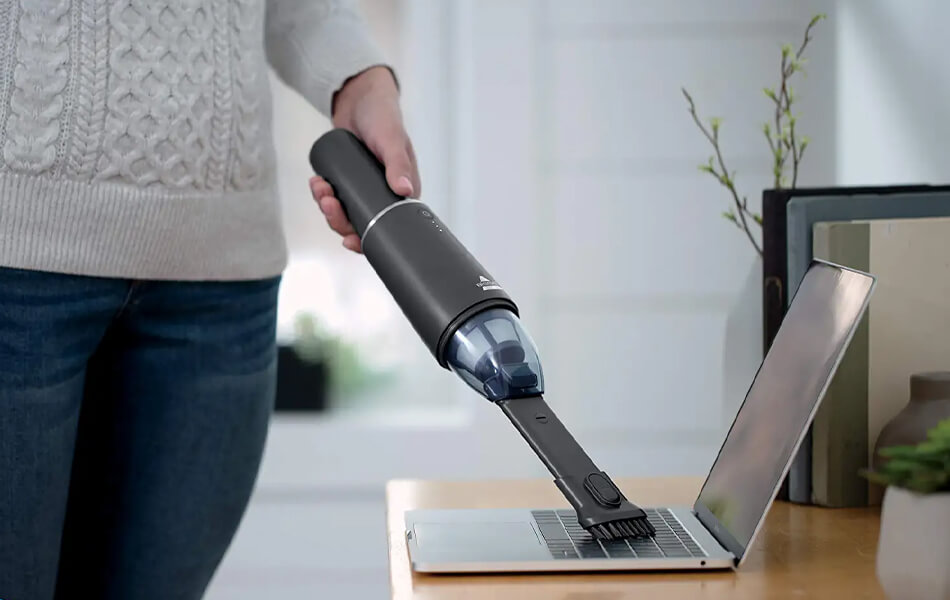 woman using handheld vacuum to clean the laptop